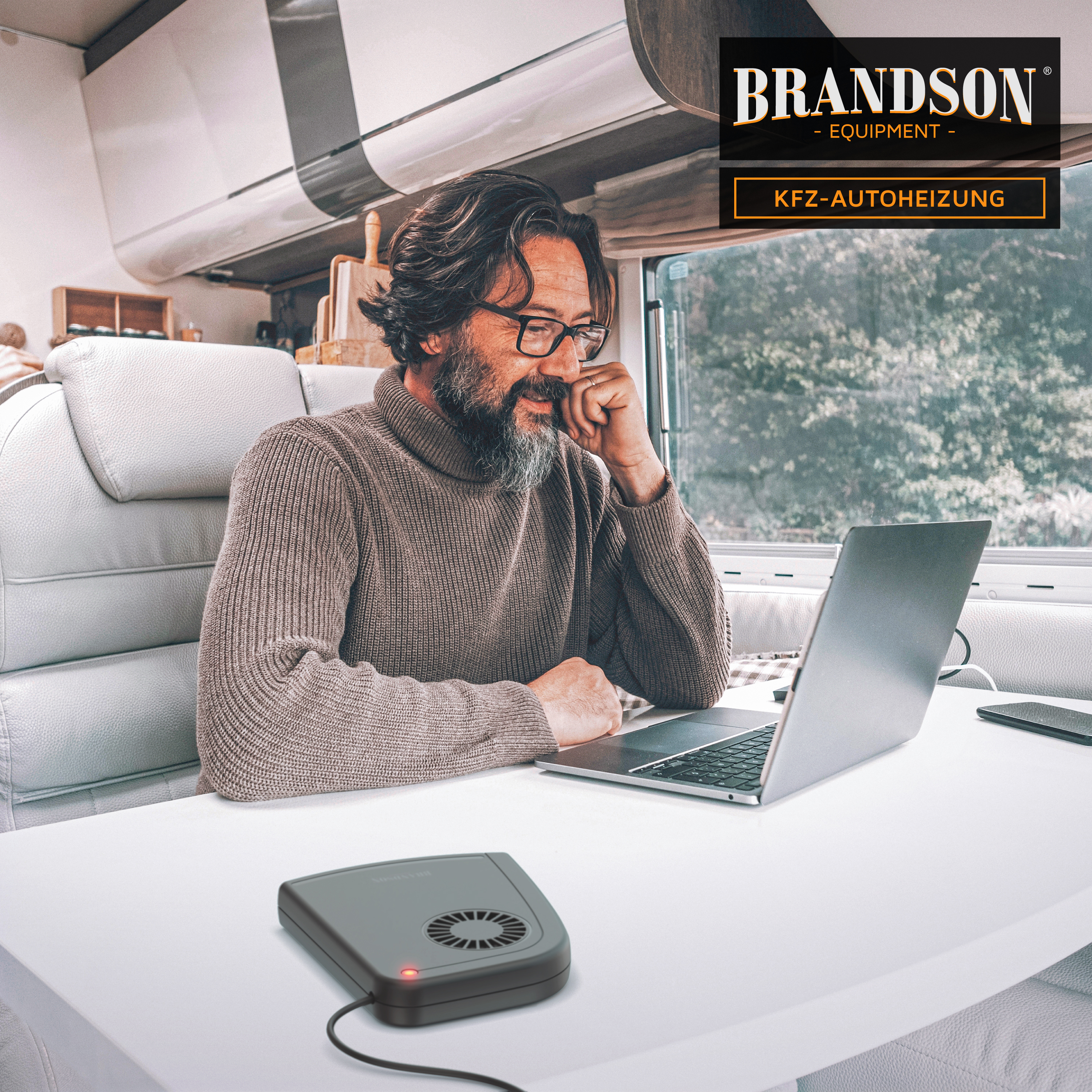 Brandson KFZ-Autoheizung in kompaktem Design, graue Farbe, mit sichtbarem Lüfter und rotem Betriebslicht, auf einem Tisch neben einem Laptop.
