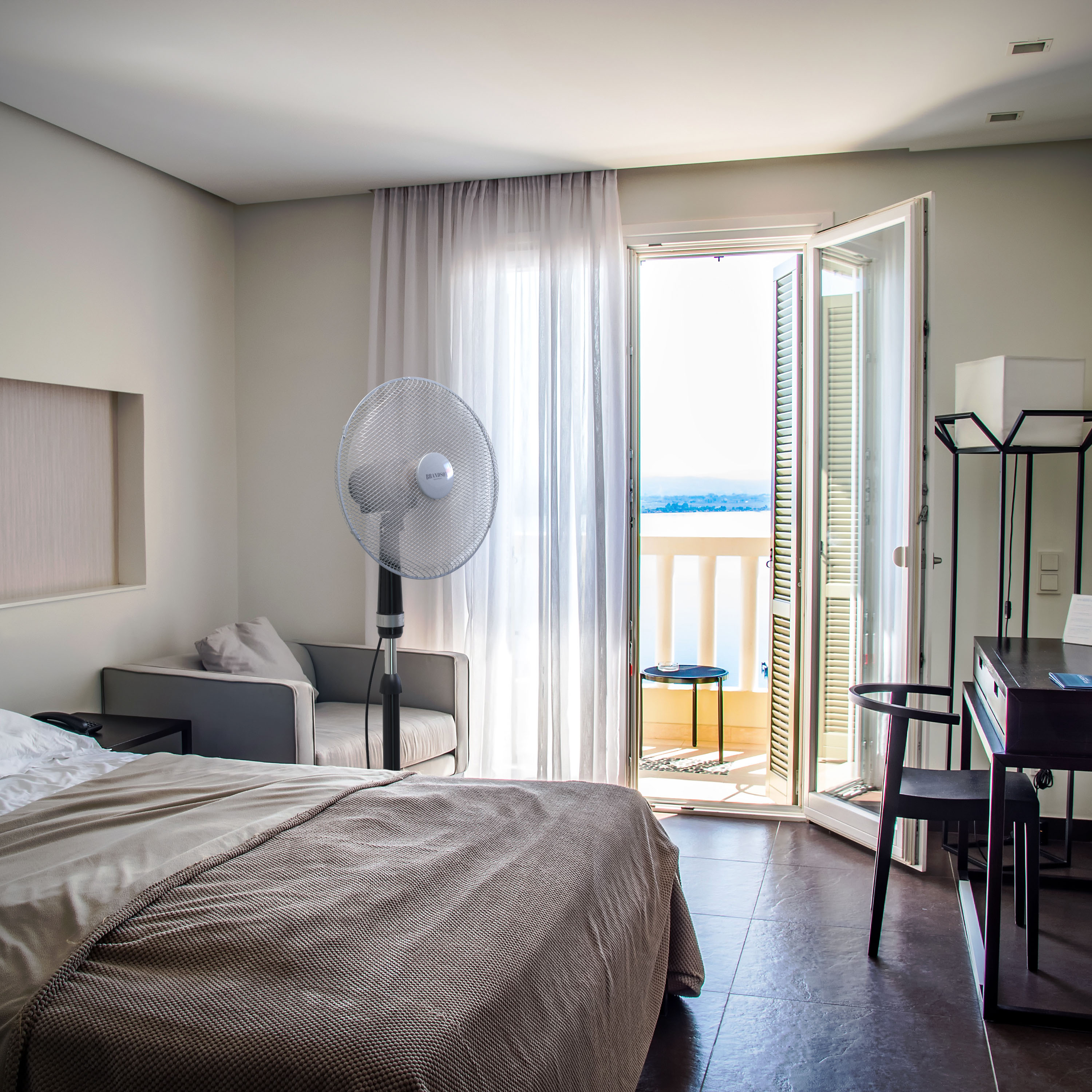 Brandson Standventilator in einem modernen Schlafzimmer, silberne Bauform mit einem stabilen Standfuß und einem transparenten Schutzgitter.