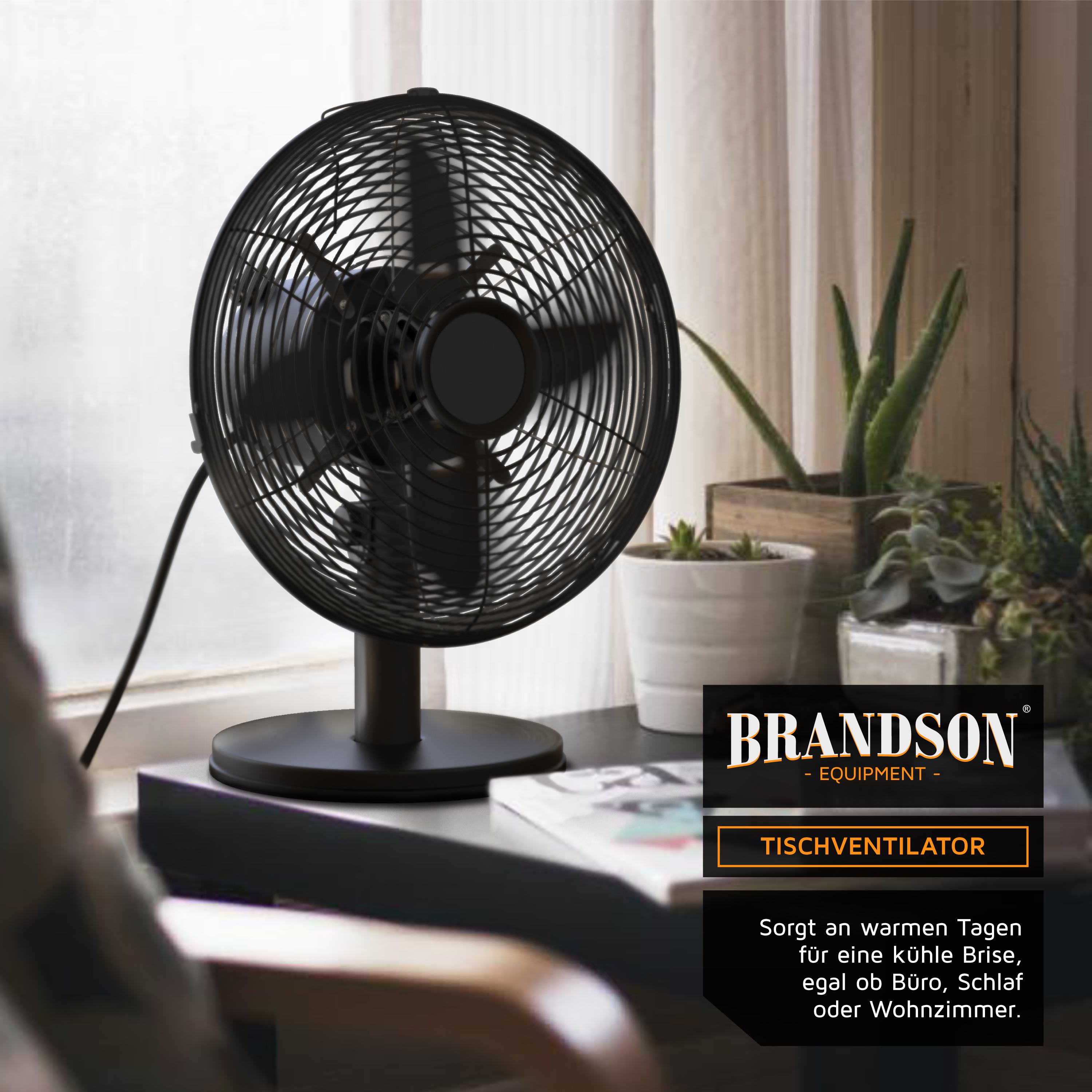 Tischventilator Brandson mit schwarzem Metallrahmen und Schutzgitter, aufgestellt auf einem Tisch in der Nähe von Pflanzen und einem Fenster.