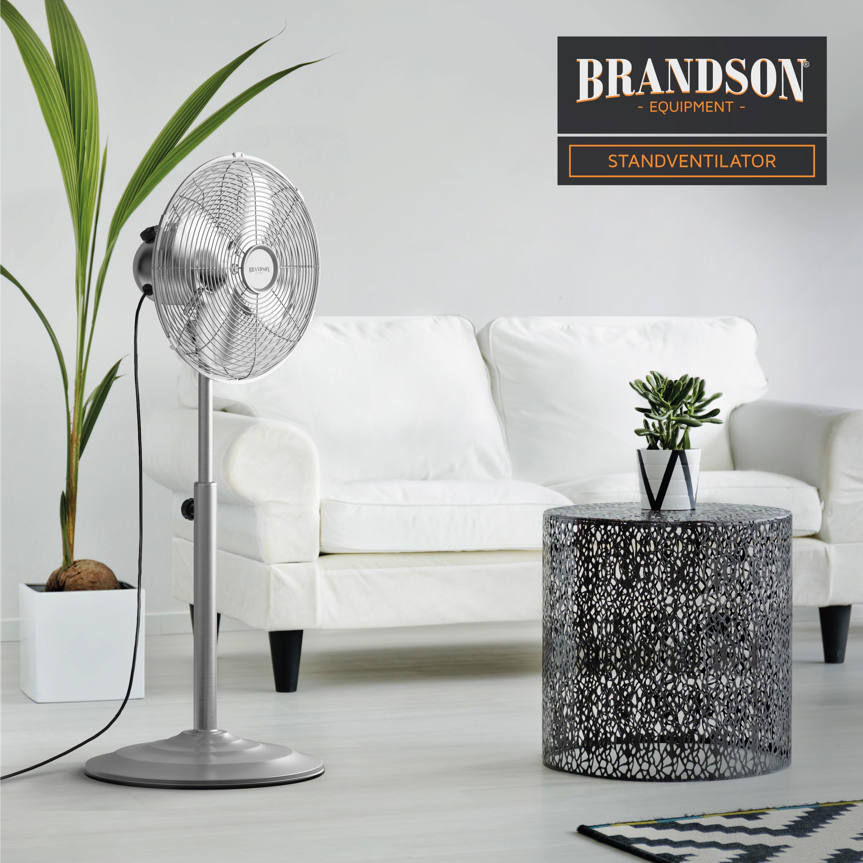 Brandson Standventilator mit Metallic-Finish und stabilem Sockel, positioniert neben einer weißen Couch und einem dekorativen Tisch.