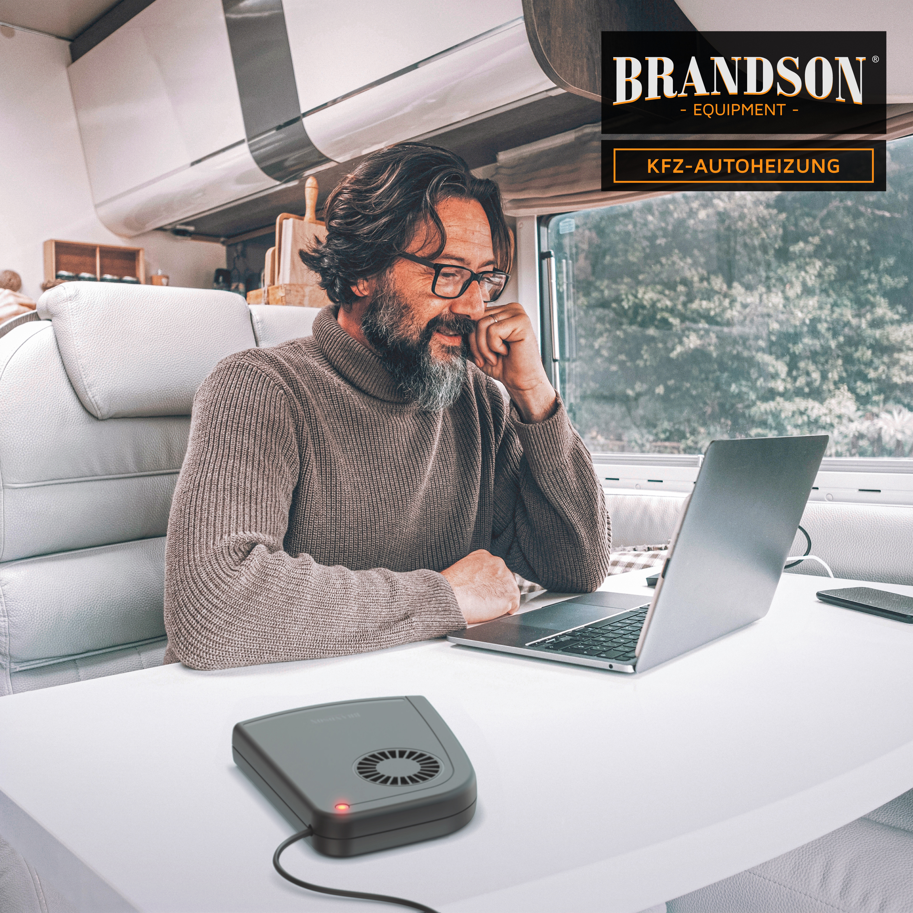 Brandson KFZ-Autoheizung in grauem Gehäuse mit Lüftungsschlitzen, auf einem Tisch neben einem Laptop, in einem Wohnmobil.