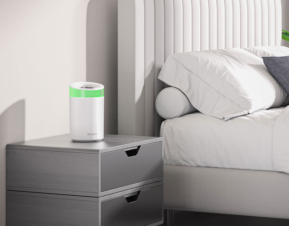 Brandson Luftreiniger in Weiß mit grünem Akzent auf einem Nachttisch neben einem Bett, ideal für die Schlafzimmernutzung.