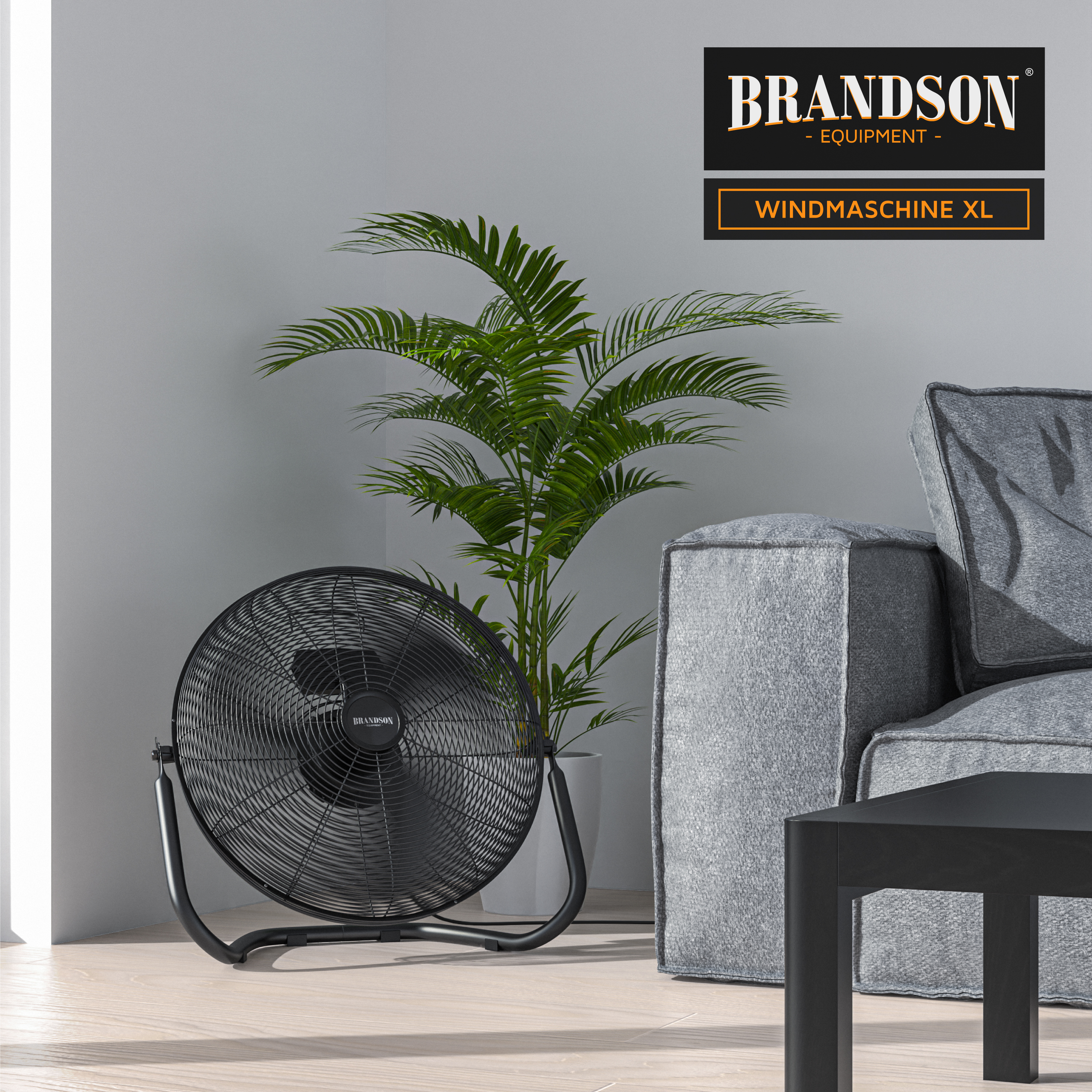 Brandson Windmaschine XL in Schwarz mit stabiler Metallbasis, auf einem hellen Boden neben einem Sofa und einer Pflanze platziert.