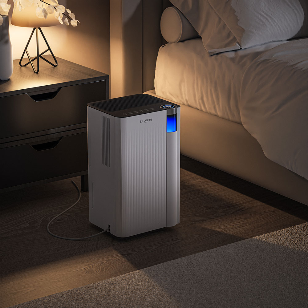 Brandson Luftreiniger im modernen Design mit blauer LED-Anzeige, platziert neben einem Bett und Nachttisch.