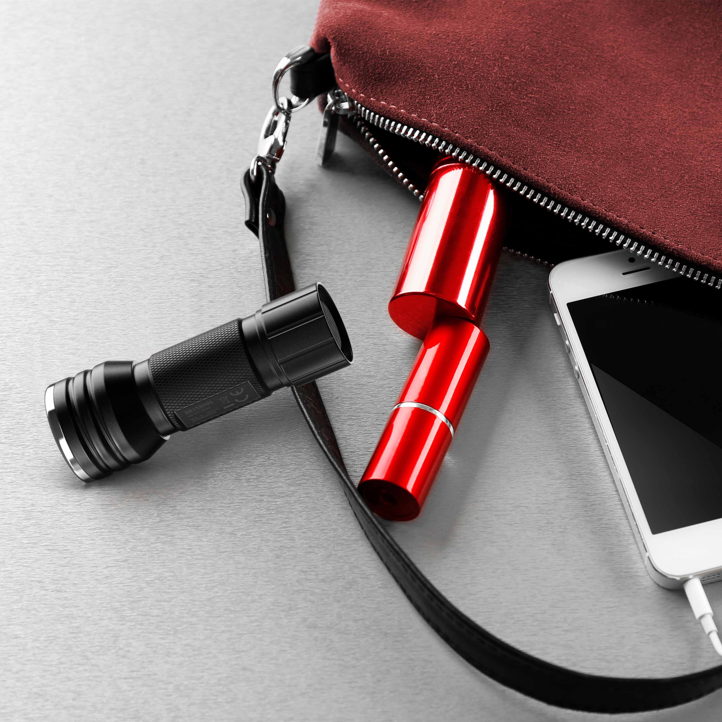 Brandson Taschenlampe in Schwarz neben rotem Lippenstift und Smartphone, teilweise aus einer Handtasche sichtbar.