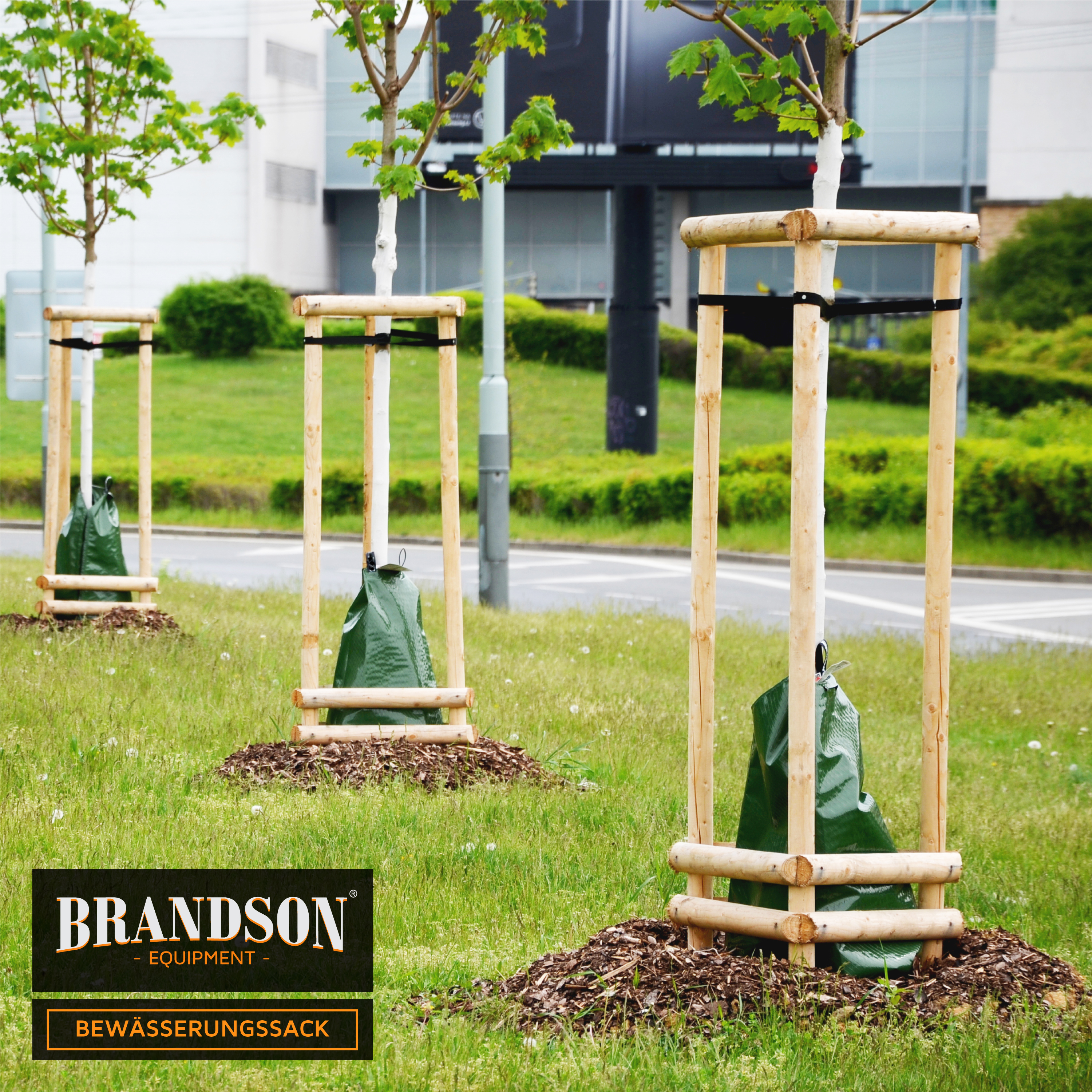 Brandson Bewässerungssack aus grünem Material, befestigt an einem Holzgestell, zur Bewässerung von Bäumen im Freien.