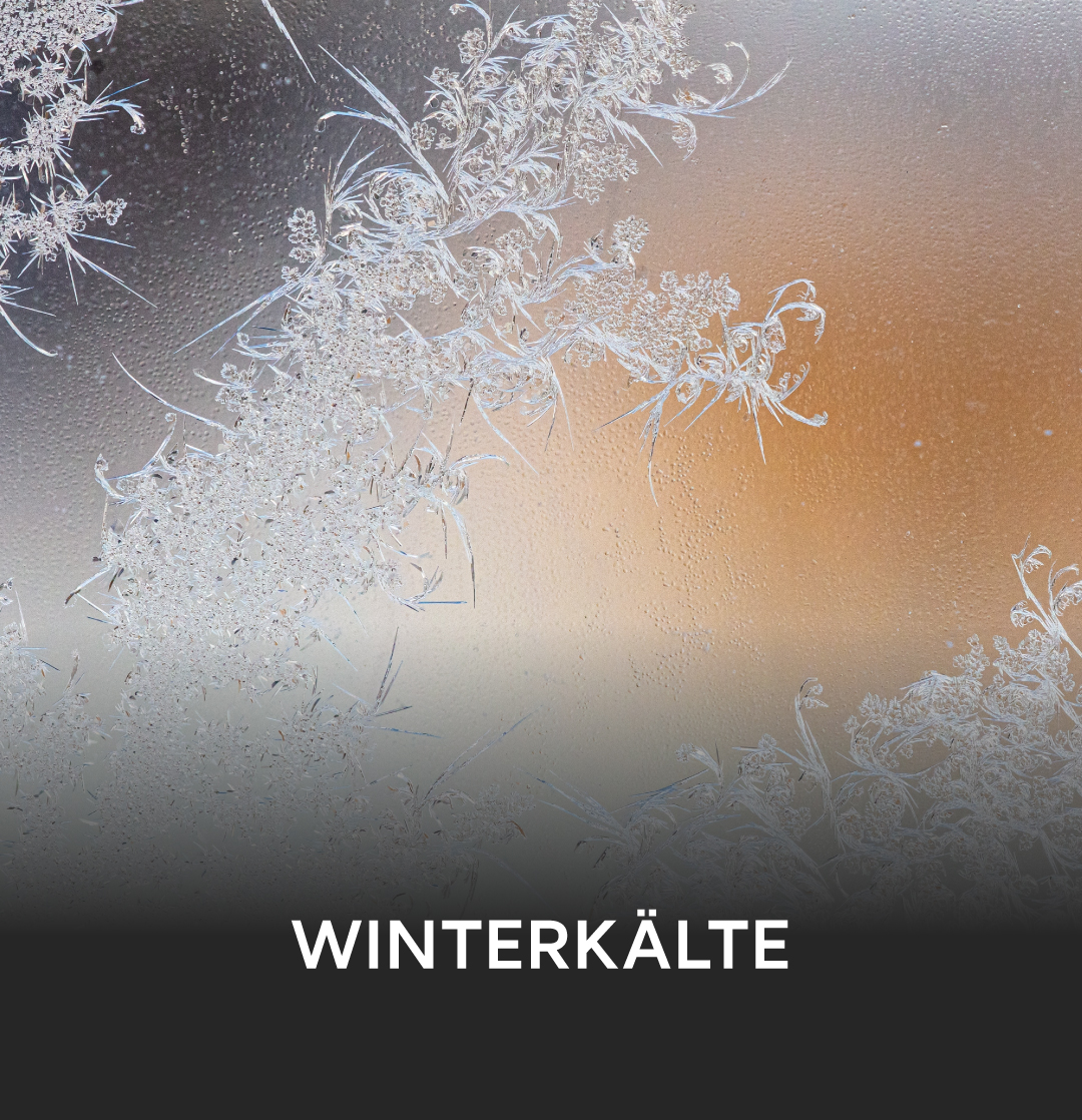 Frostige Winterkälte mit filigranen Eiskristallen auf einer Glasoberfläche, die einen warmen Hintergrund zeigt.