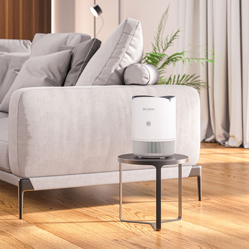 Brandson Luftreiniger in Weiß mit runder Form, auf einem Tisch neben einem grauen Sofa platziert, ideal für Wohnräume.