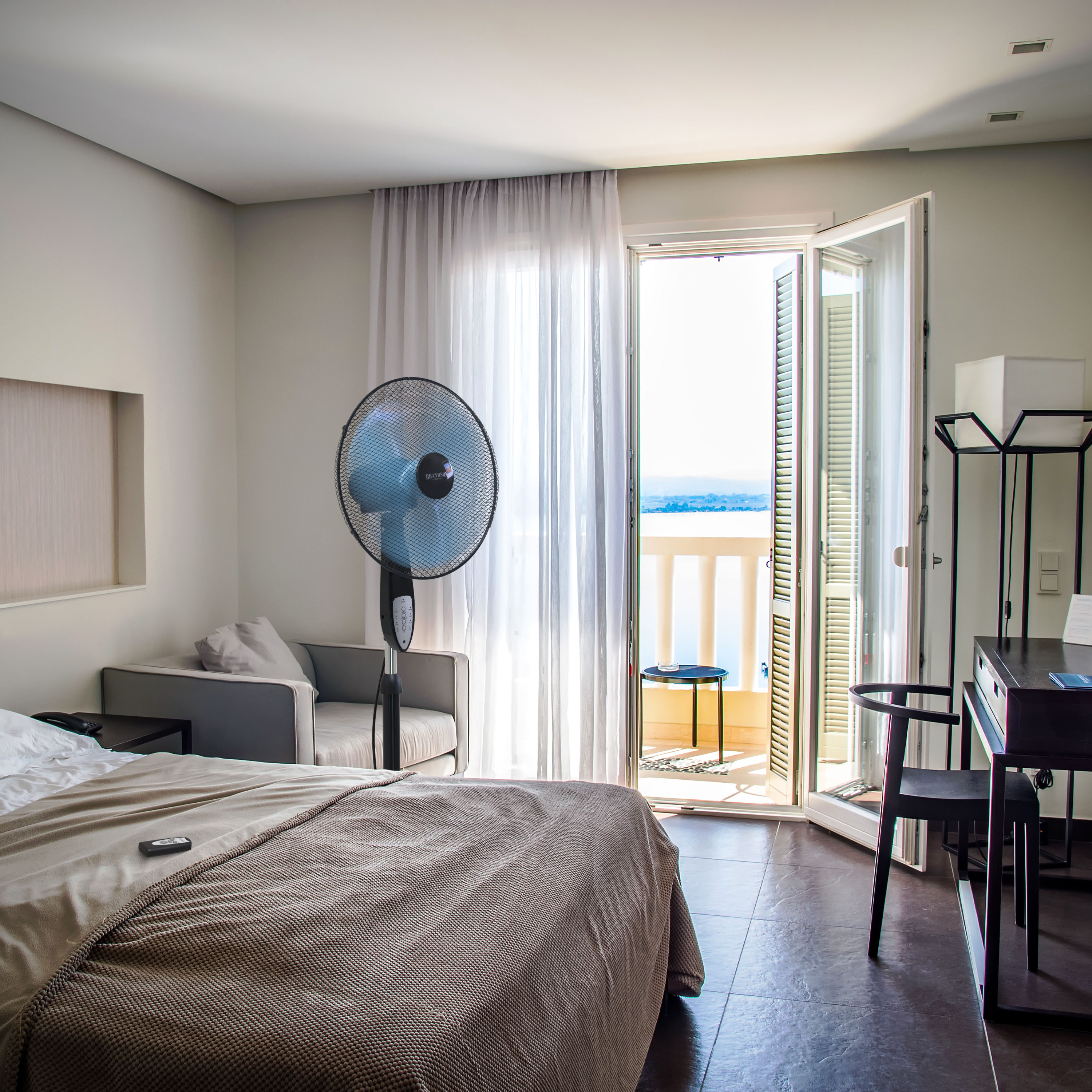 Brandson Standventilator in einem modernen Zimmer mit Bett und Balkon, mit elegantem Design, schwarzen und silbernen Farben und Fernbedienung.